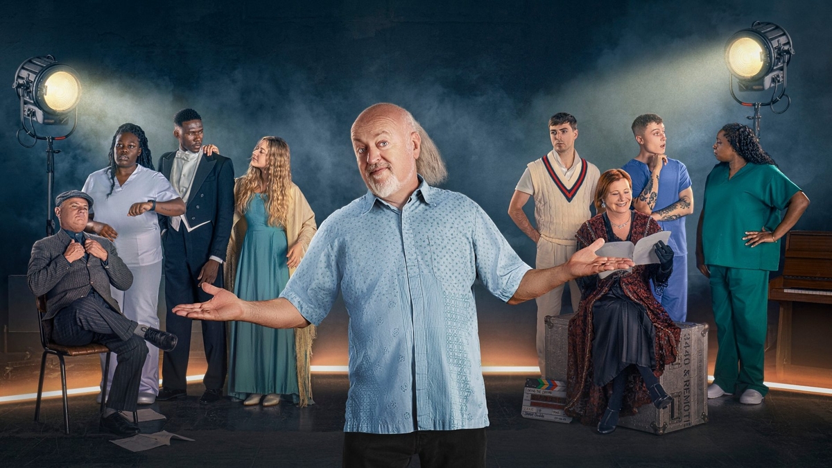 Bill Bailey stands in front of actors, who are themselves in front of two large studio lights