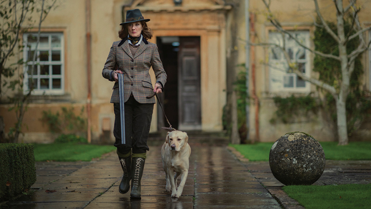 A woman walks a dog in front of a lavish house