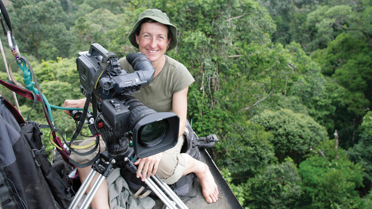 A woman sits with a camera, high up in the trees