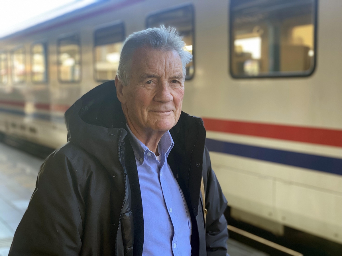 Grey haired man stands in next to a train on train platform in train station